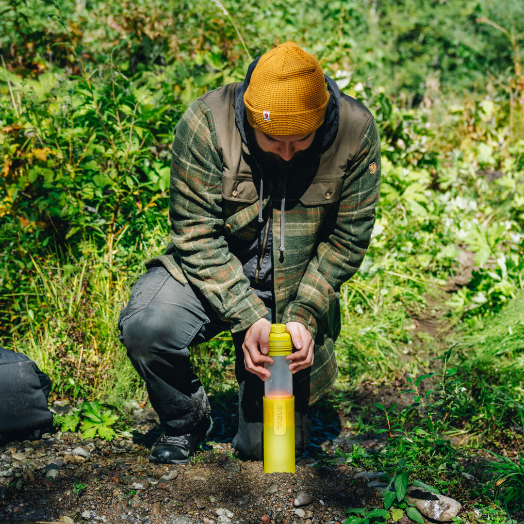 man kneeling and pressing down on the top of his Grayl with two hands