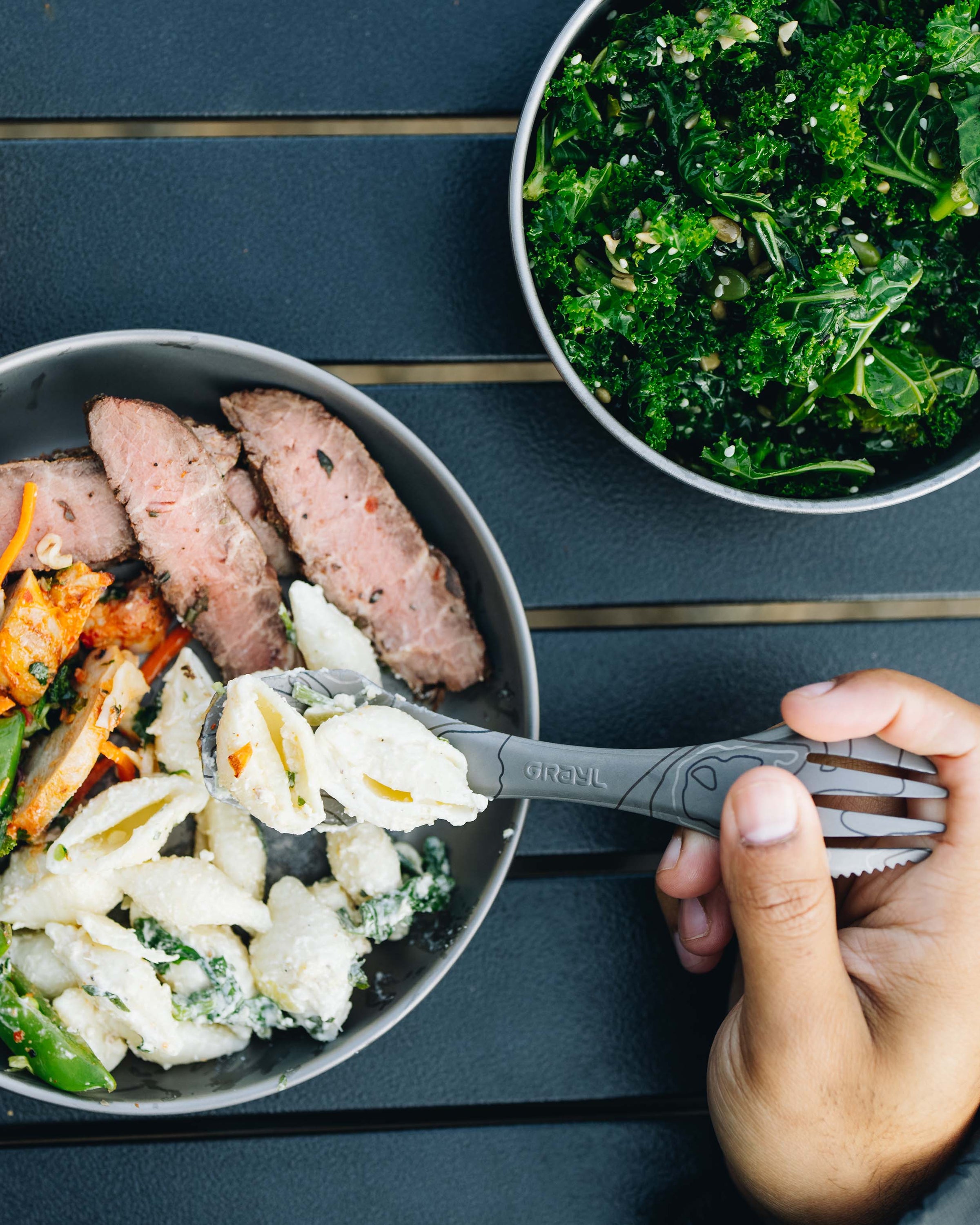 Eating steak, macaroni, and kale salad served on titanium dining set