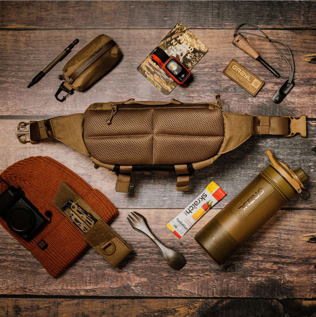 Flat lay on wood depicting air mesh back of 4L Grayl Transport Hip Pack in Coyote Brown. Grayl G-MOD Pod and Multi-Tool Pouches also visible as well as Grayl patch.