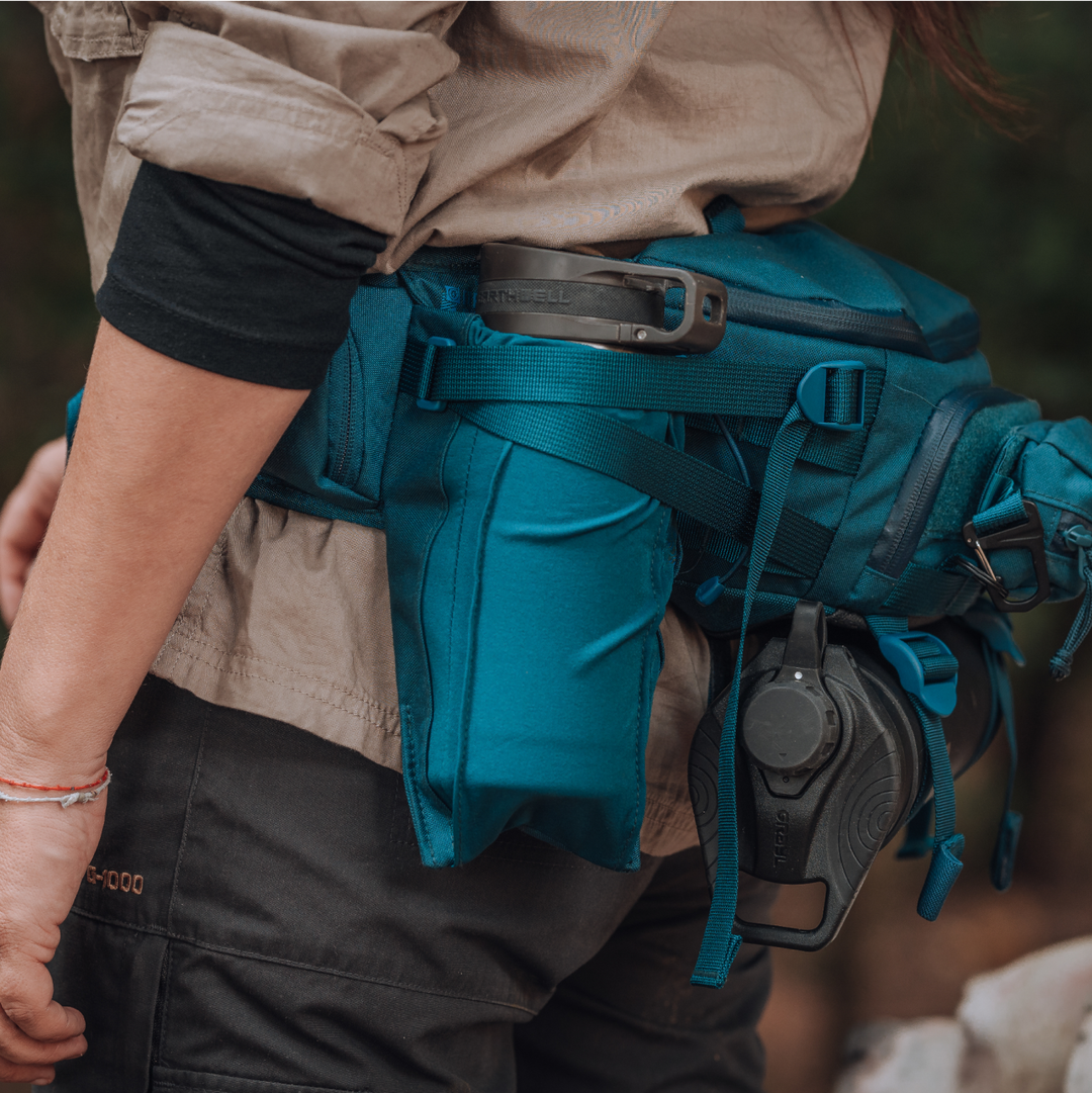 Woman in Fjallraven G-1000 pants wearing a Grayl® Mission Hip Pack in Wander Blue colorway. Stainless steel double-wall insulated Earthwell® water bottle featured in Expanse BottleDrop™ Pocket. G-Mod Pod Pouch and GeoPress® Titanium Black Edition attached to hip pack.